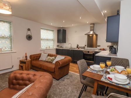 An open plan living room and kitchen with brown sofas a dining table set for breakfast and dark kitchen cabinets at Stowaway Cottage in Whitby