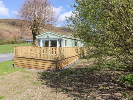 A green mobile home with wooden deck fencing in a rural area with hills and trees at Whiteside in Lorton