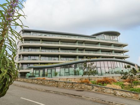 A modern multi-story building with balconies and glass railings near a road with a stone wall and plants at Sebastian's View in Falmouth