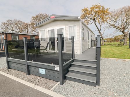 A mobile home with a glass railing deck and stairs on a gravel and grass lot at Lodge 7 - Seabreeze Retreat in Bridlington