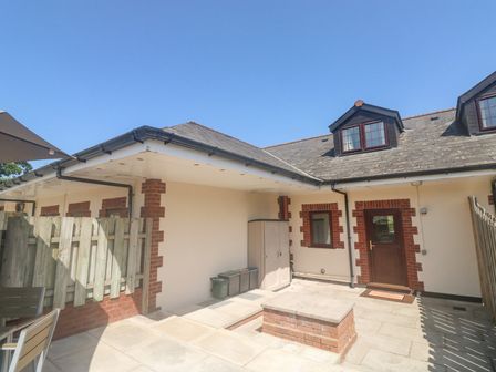 A courtyard with paved floor a wooden door windows and storage units at Kingfisher Cottage in Bottreaux Mill near South Molton