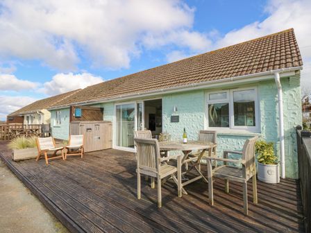 An outdoor wooden deck with chairs and a round table outside a light blue house at Little Beach in Seaview
