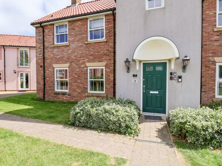 Exterior of a brick and stucco house with a green front door and pathway surrounded by grass and bushes at Kittiwakes The Bay - Filey