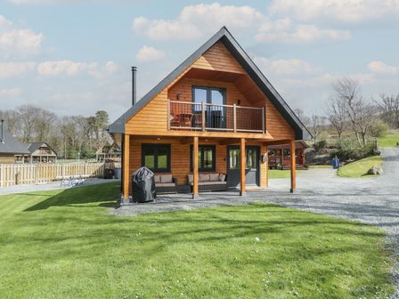 A wooden two-story house with a balcony and outdoor seating on the lawn at Sunset Lodge 5 in Llanbedr