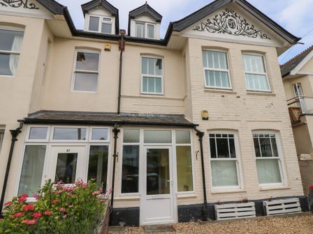 Front view of a two-storey house with white framed windows and doors with flowering bushes in front at Chine Heights in Bournemouth