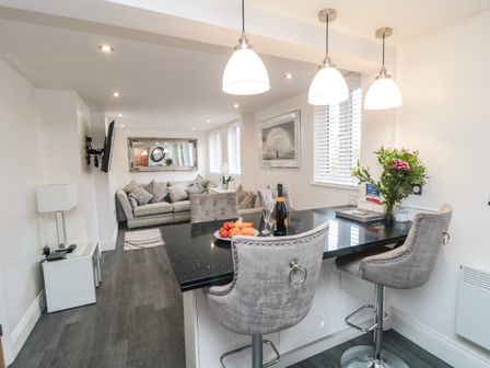 A kitchen island with two bar stools and a vase of flowers next to a living room with a sofa and a wall-mounted television at Tower Apartment in Whitby