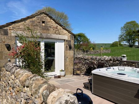 An outdoor patio with a stone wall a hot tub a small table with two chairs and a stone house at The Folly in Linton near Thresfield