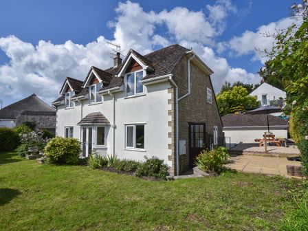 A two-story house with a garden and patio area with a picnic table and umbrella at Fawley in Lyme Regis