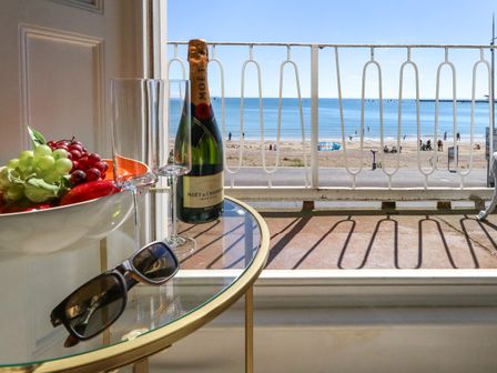 A glass table with sunglasses fruit bowl champagne bottle and glasses overlooking a beach and sea at 123 On The Sea in Weymouth