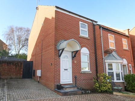 A brick end terrace house with a white door and windows and a paved driveway at The Nightingale in Weymouth