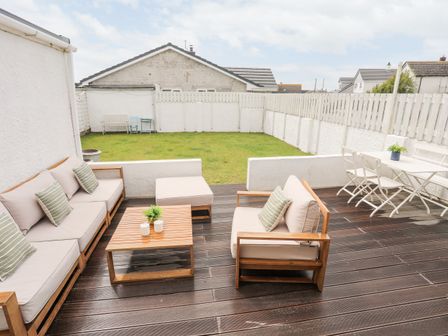 A backyard with wooden deck furniture and a grassy lawn at 31 Sisial Y Mor in Rhosneigr