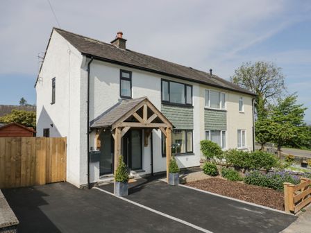 A two-story semi-detached house with a wooden porch and two potted plants at Ananda House in Windermere