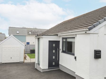 The exterior of a white house with a dark gray front door and a garage with a white door at Clydfan No 1 Trearddur Road in Trearddur Bay