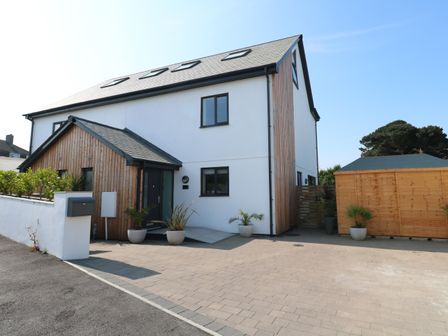 A modern white house with wooden panels and a driveway with potted plants and a wooden shed at Lamorna in Praa Sands