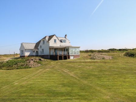 A detached house with a porch and glass conservatory surrounded by grass at Wig Carna in Holyhead