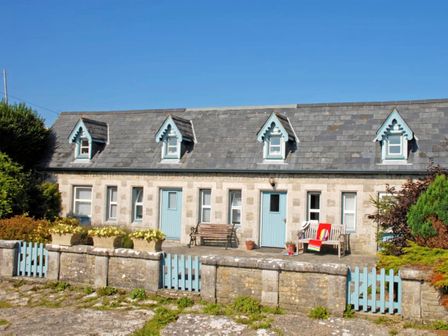 A stone cottage with blue doors and dormer windows with planters on the wall and benches outside at The Hen House Southerndown near St Brides Major