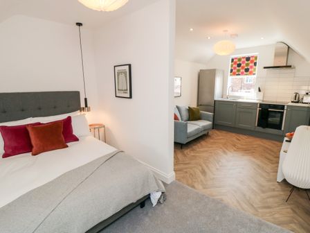 A bedroom with a bed and cushions next to a kitchen and living area with a sofa and refrigerator at The Salthouse Apartment 3 in Scarborough