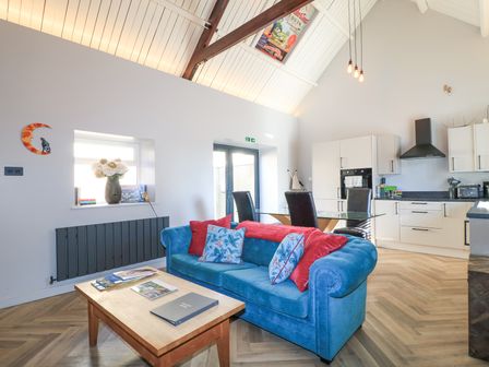 An open plan living room and kitchen with a blue sofa and glass dining table at Mayfield Cottage in Nr Malmesbury