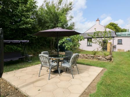 An outdoor patio area with a table, chairs, and umbrella adjacent to a house with a garden at The Old Forge Cottage in Kilkhampton