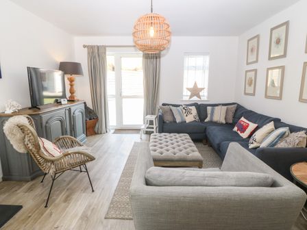 A living room with a corner sofa, armchair, ottoman, television on cabinet, and framed pictures on the wall at Llwyn Onn in Morfa Nefyn