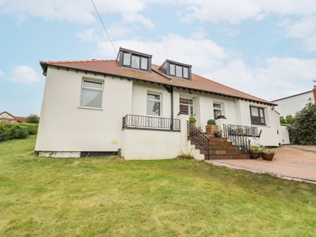 A house with dormer windows a grassy front yard and stairs leading to the entrance at Pine Lodge in Colwyn Bay
