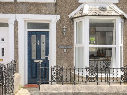 Front door and bay window of a house with a metal fence in front at Maes Y Ddol in Nefyn