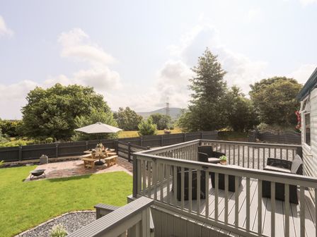 An outdoor patio with chairs and a table and a garden area with a wooden picnic table and umbrella at Tyn Clwt in Penisa'r Waun near Llanrug