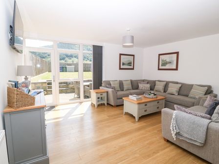 A living room with a large gray sectional sofa and wooden coffee tables near glass doors opening to a garden at 3 Pensyflog Barns in Porthmadog