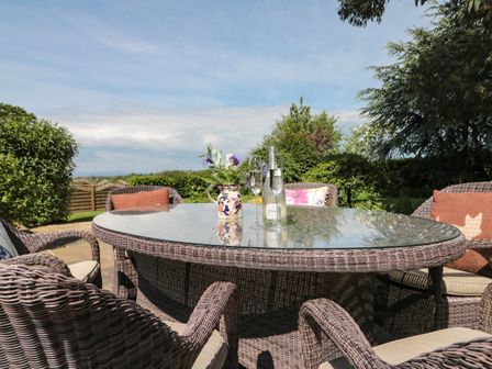 An outdoor patio area with a glass topped wicker table and wicker chairs with cushions at The Old Dairy in Sutton near Thirsk