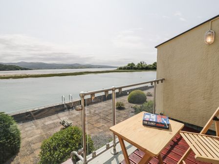 A balcony with a wooden table and chair overlooking a river and distant hills at 25 South Snowdon Wharf in Porthmadog