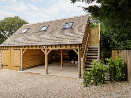 A wooden garage with two open parking bays and stairs leading to an upper floor at The Rookery in Fulbrook near Burford