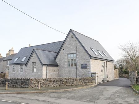 A stone building with a slate roof and multiple windows surrounded by a stone wall at Ysgol Fawr Big School in Benllech