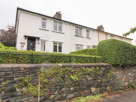A row of white houses with black doors behind a stone wall and green hedges at 1 Millbank in Keswick