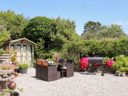 An outdoor patio with a garden table and chairs a barbecue and a small green shed surrounded by plants at The Attic in Ruan Minor