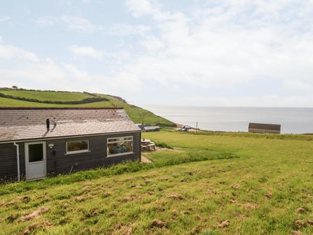 A coastal landscape with a building on grassy land overlooking the sea at Siesta Chalet in Eype Mouth Chalet Park