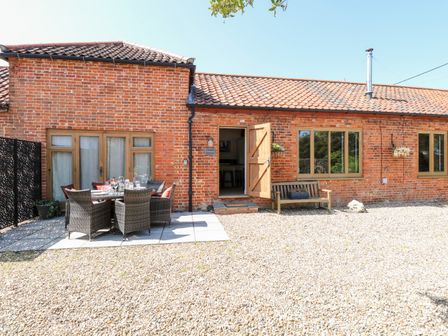 An outdoor patio area with a dining table and chairs and a wooden bench against a brick building at The Barnhouse Felmingham near North Walsham