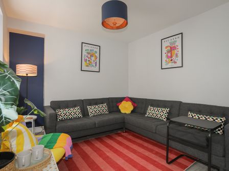 A living room with a gray sectional sofa colorful cushions a red striped rug and two Picasso art prints on the wall at Gwynle in Nefyn