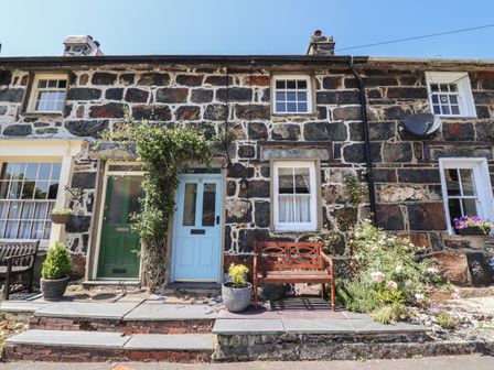 Stone cottage exterior with two front doors and a wooden bench with plants in Beddgelert