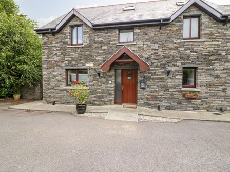 Stone exterior of a house with four windows and a wooden door with a small porch at 1 The Courtyard in Durrus County Cork