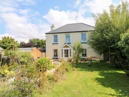 A two story cream house with a sloped roof and a garden in front at Pentira in Kuggar