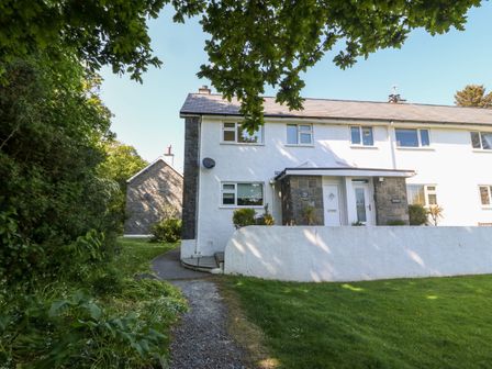 An exterior view of a white residential building with a garden and trees at 20 Glyn Y Mor in Llanbedrog