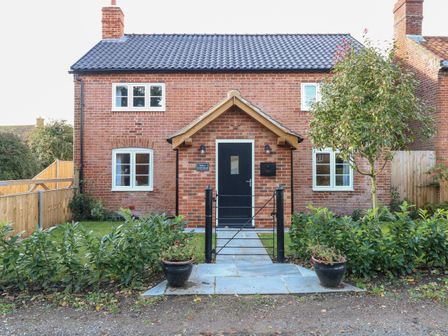 A brick house with a black door and two chimneys with plants and a tree in the garden at Well Cottage in Seething near Loddon