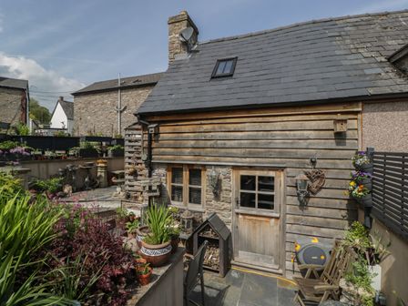 A garden area with plants in pots and a wooden building with a door and window at Hoarders Cottage in Hay-On-Wye