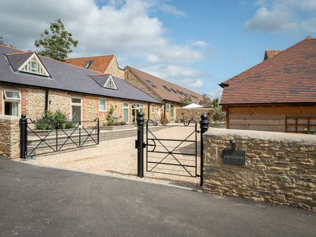 A gated entrance with stone walls and several stone buildings with slate and tile roofs at The Stables in Wheatley