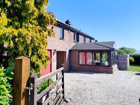 A brick house with a conservatory and wooden gate on a gravel driveway at Yewtree House in Sockbridge near Askham Cumbria