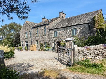 A stone farmhouse with a gravel driveway a wooden gate and garden at The Dairy at Brackenthwaite Farm in Arnside