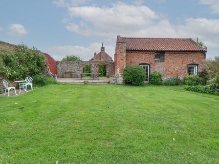 A garden with a patio area and outdoor furniture next to a brick building at Pear Tree Barn in Stalham
