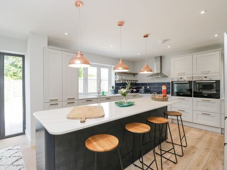 A kitchen with a large island and four stools under copper pendant lights at Greystones in Upton St Leonards