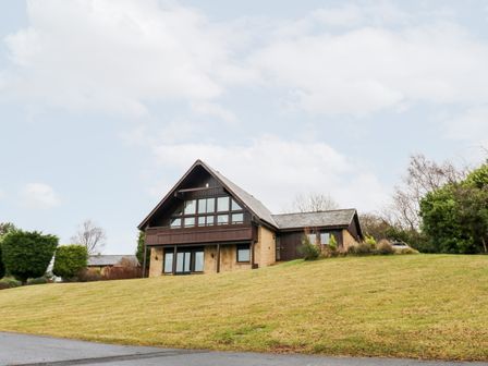 A house with a steep roof and large windows on a grassy hill with trees in the background at Slaley Park Villa in Hexham