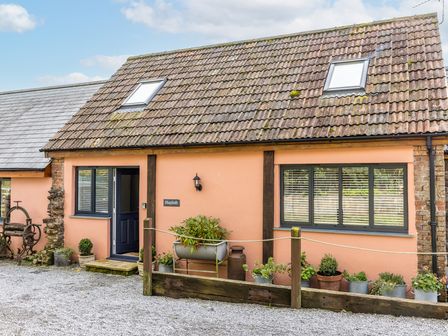Exterior view of a single-story building with tiled roof windows a door and plants in pots at The Hayloft in Bampton Devon